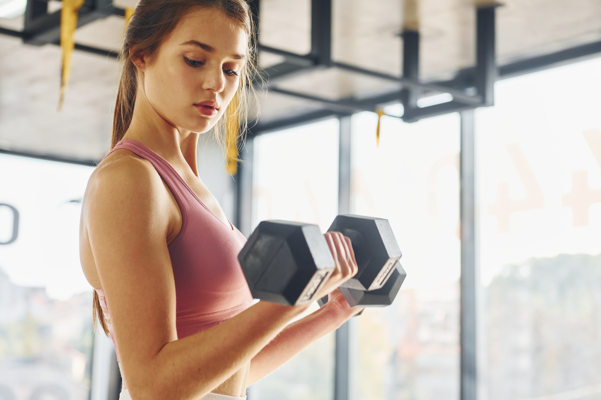 Focused on exercise. Beautiful young woman with slim body type is in the gym